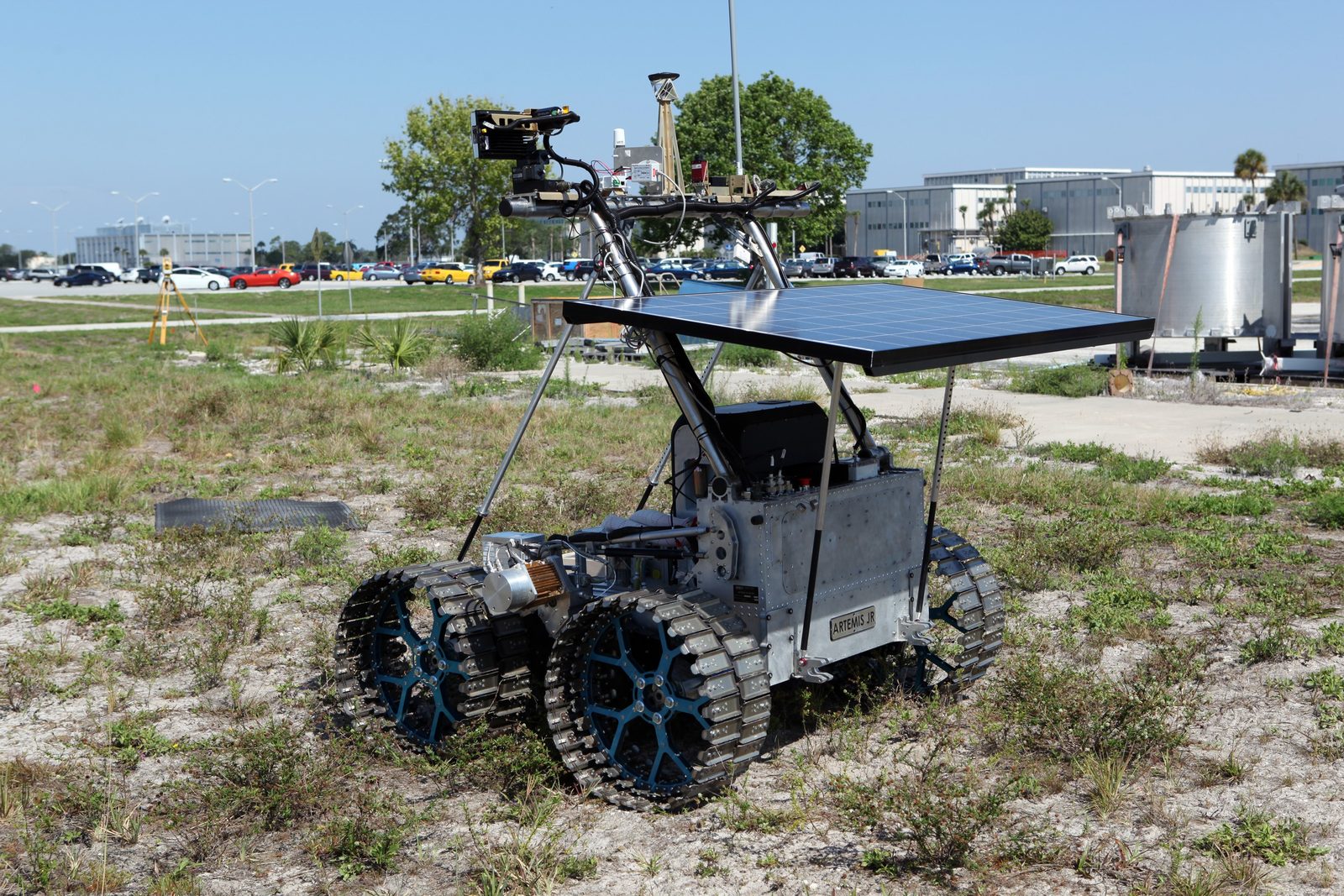 The four-wheeled Artemis Jr. prototype rover, topped with a solar array, driving across a grass field beside the Operations and Checkout Building. Real NASA photograph used on the Ellis Abel Learns "Why I Love Cars" page.