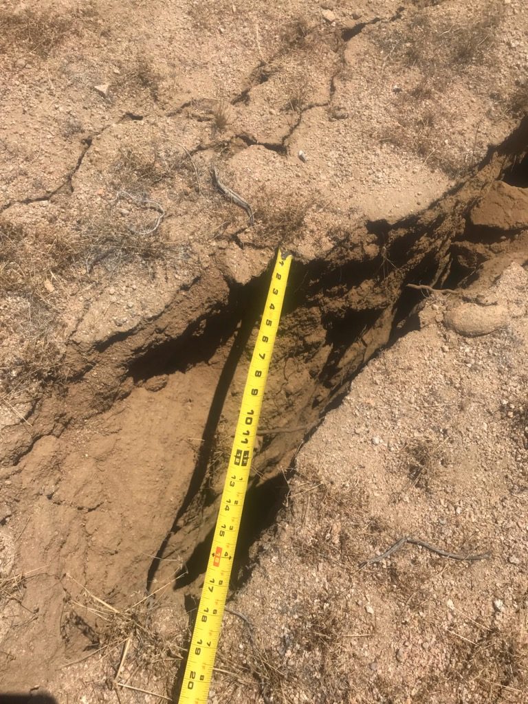 A jagged crack running across desert ground with a yellow tape measure stretched over it, marking surface rupture from the 2019 Searles Valley earthquake. Real USGS photograph used on the Ellis Abel Learns "Why I Love Earthquakes" page.