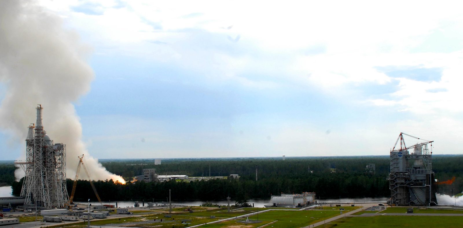 Two rocket engine tests fire at once on the test stands at Stennis Space Center, throwing huge white exhaust plumes into the air. Real NASA photograph used on the Ellis Abel Learns "Why I Love Energy" page.