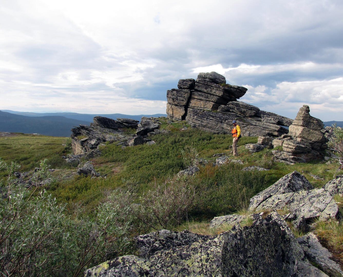 A USGS scientist stands against a folded, strongly deformed rock face on Divide Mountain, Alaska, examining the layers up close. Real USGS photograph used on the Ellis Abel Learns "Why I Love Geology" page.