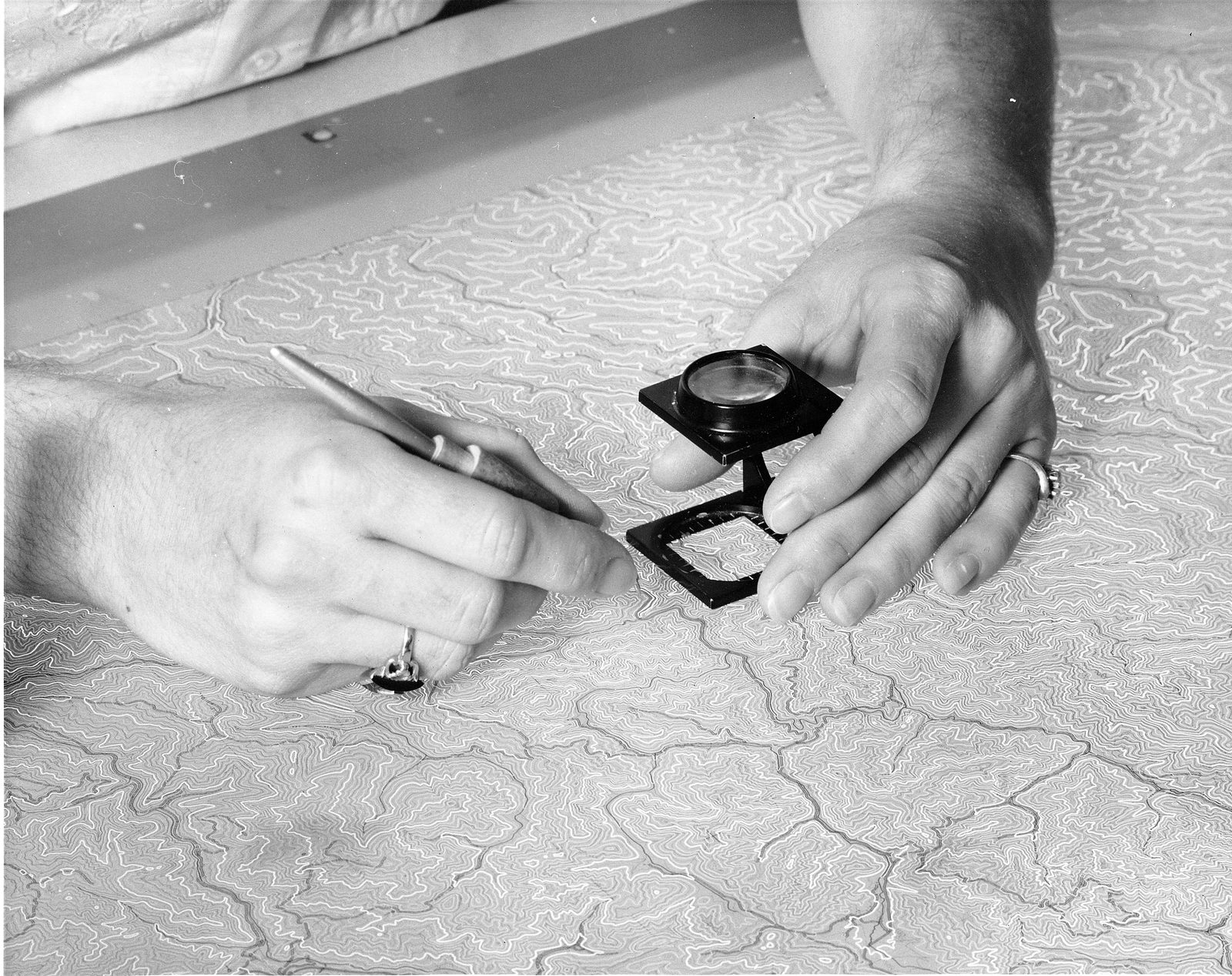 A USGS cartographer bends over a light table, scribing contour lines by hand onto a topographic map separation. Real USGS photograph used on the Ellis Abel Learns "Why I Love Maps" page.