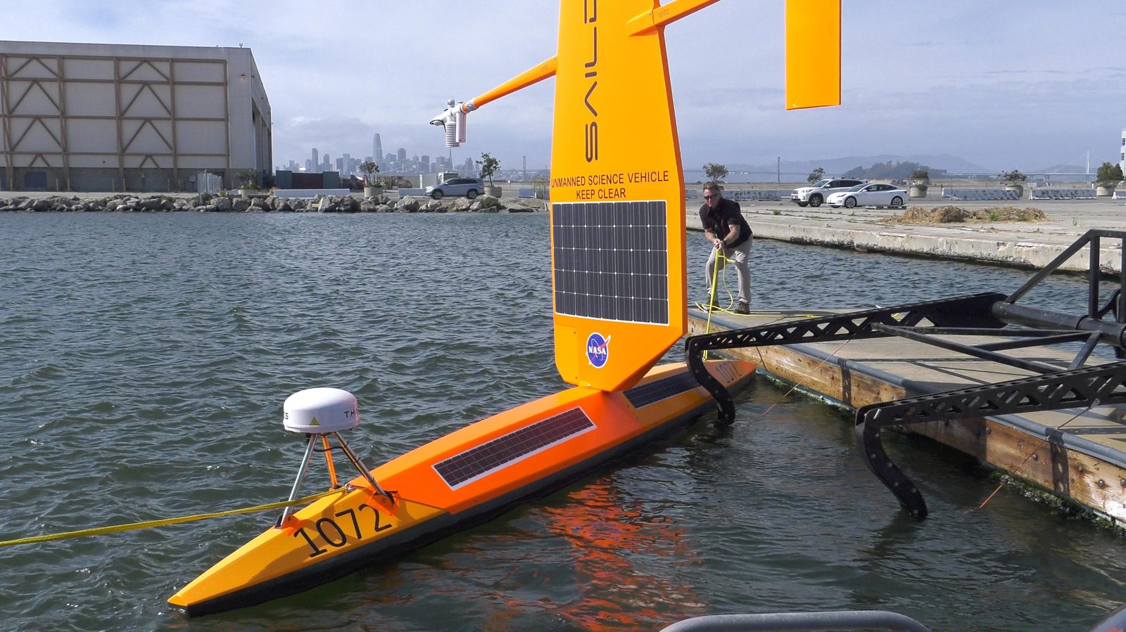 An orange-and-white Saildrone autonomous research vessel under sail on the water near San Francisco Bay. Real NASA photograph used on the Ellis Abel Learns "Why I Love Oceans" page.