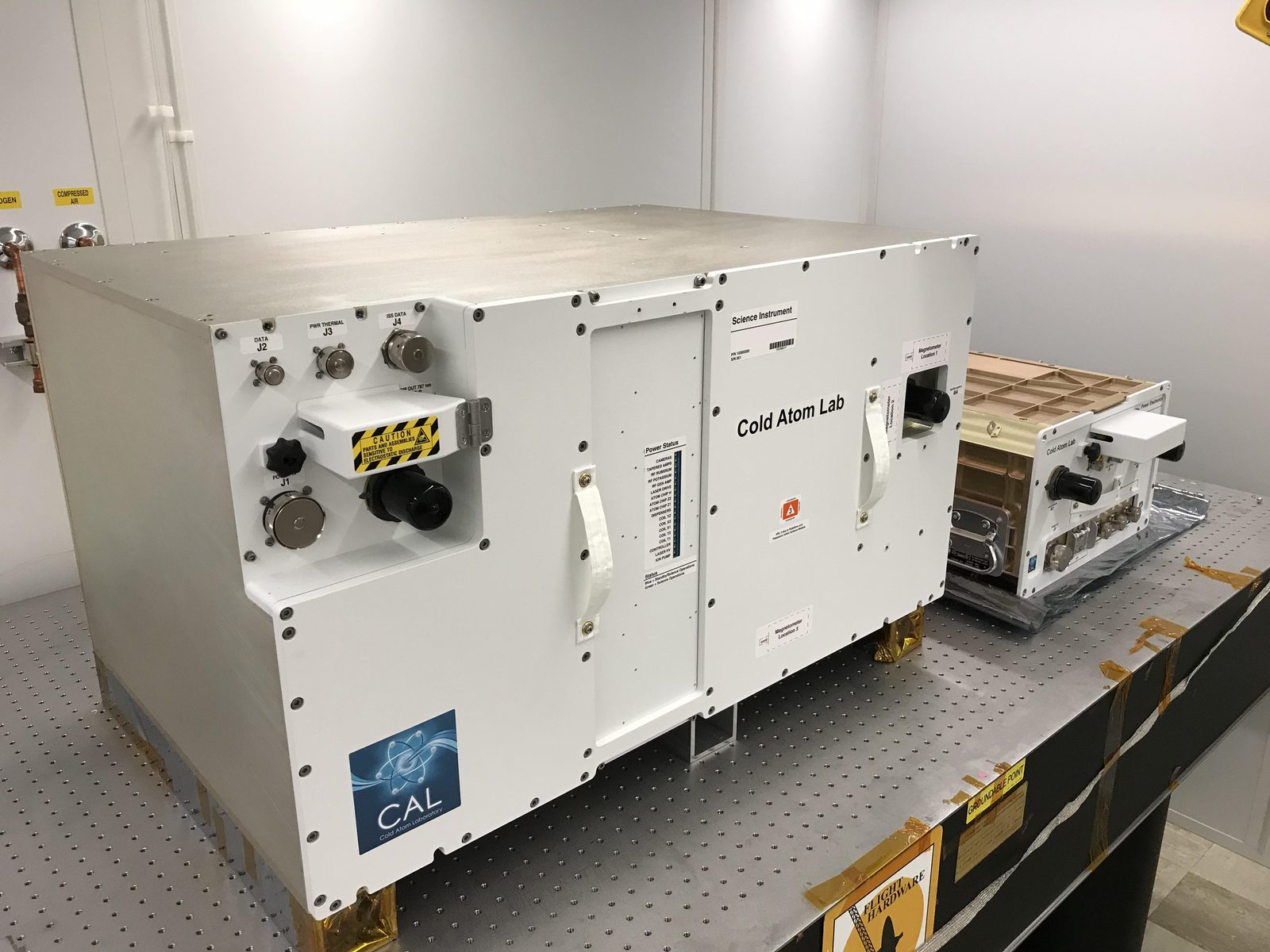 The Cold Atom Laboratory, two white equipment containers packed with lasers and vacuum hardware, on a bench before flight. Real NASA photograph used on the Ellis Abel Learns "Why I Love Physics" page.