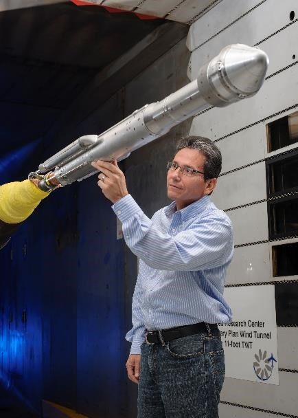 Someone working in Planes — Ellis Abel Learns An engineer reaches into a wind tunnel at Ames Research Center to adjust a scale model of an Atlas V rocket with a Starliner capsule. Real NASA photograph used on the Ellis Abel Learns "Why I Love Planes" page.