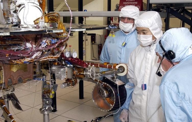 Someone working in Robotics — Ellis Abel Learns JPL engineers lean over the folded robotic arm of a Mars Exploration Rover, inspecting its joints in the lab. Real NASA photograph used on the Ellis Abel Learns "Why I Love Robotics" page.