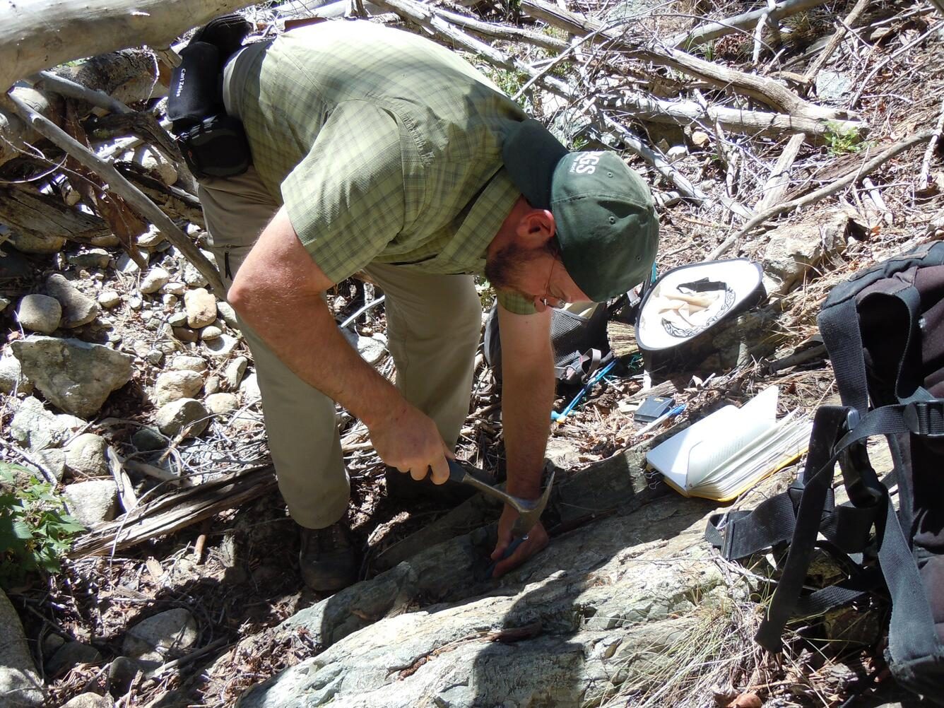 Someone working in Rocks — Ellis Abel Learns Geologist Jonathan Caine swings a rock hammer against a fault outcrop in Deadman Gulch, Colorado, to break off a sample. Real USGS photograph used on the Ellis Abel Learns "Why I Love Rocks" page.